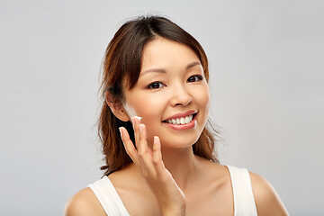 Image showing young asian woman applying moisturizer to her face