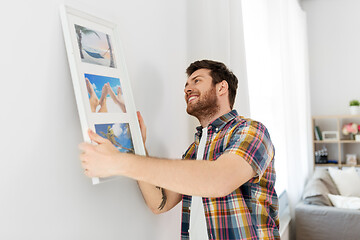 Image showing man hanging picture in frame to wall at home