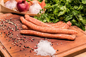 Image showing raw sausages with chilli and herbs on a wooden board with spices