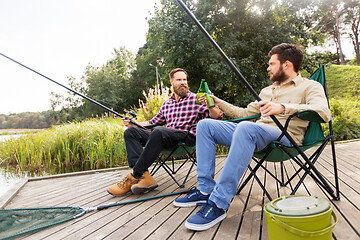 Image showing happy friends fishing and drinking beer on pier