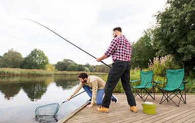 Image showing male friends with net and fishing rods on lake