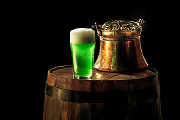 Image showing The wooden background with lots of gold coins and a large mug of beer with a green bow.