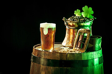 Image showing The wooden background with lots of gold coins and a large mug of beer with a green bow.