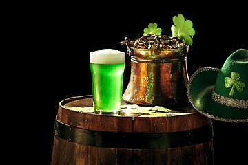 Image showing The wooden background with lots of gold coins and a large mug of beer with a green bow.