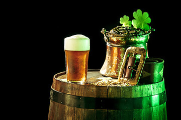 Image showing The wooden background with lots of gold coins and a large mug of beer with a green bow.