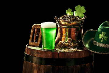 Image showing The wooden background with lots of gold coins and a large mug of beer with a green bow.