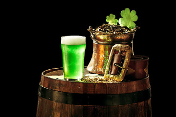 Image showing The wooden background with lots of gold coins and a large mug of beer with a green bow.