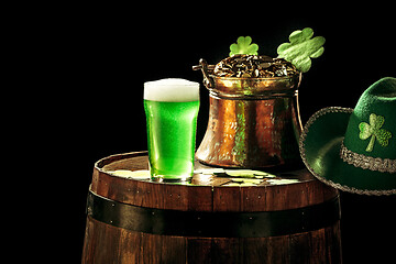 Image showing The wooden background with lots of gold coins and a large mug of beer with a green bow.