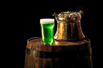 Image showing The wooden background with lots of gold coins and a large mug of beer with a green bow.