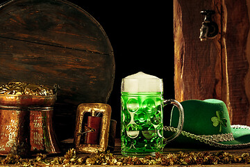 Image showing The wooden background with lots of gold coins and a large mug of beer with a green bow.