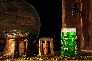 Image showing The wooden background with lots of gold coins and a large mug of beer with a green bow.