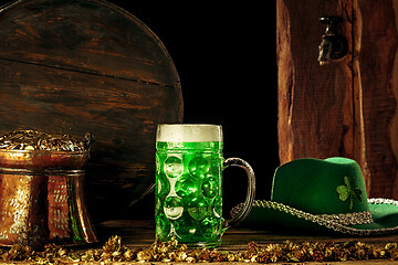 Image showing The wooden background with lots of gold coins and a large mug of beer with a green bow.