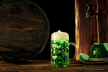 Image showing The wooden background with lots of gold coins and a large mug of beer with a green bow.