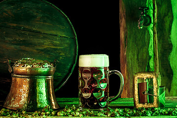 Image showing The wooden background with lots of gold coins and a large mug of beer with a green bow.