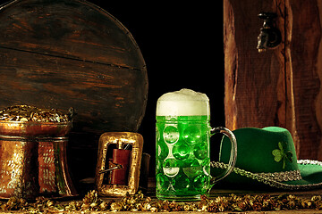 Image showing The wooden background with lots of gold coins and a large mug of beer with a green bow.