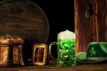 Image showing The wooden background with lots of gold coins and a large mug of beer with a green bow.