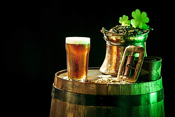 Image showing The wooden background with lots of gold coins and a large mug of beer with a green bow.