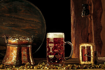Image showing The wooden background with lots of gold coins and a large mug of beer with a green bow.
