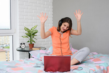 Image showing The girl is funny and welcoming waving her hands while looking at the laptop screen