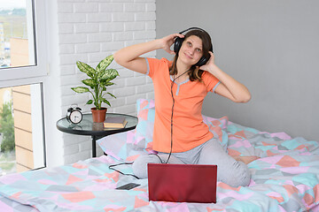 Image showing The girl put on her headphones, connected them to the computer and is listening to music happily