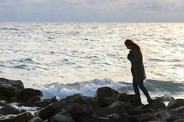 Image showing Lonely girl in a depressed mood walking along a rocky seashore