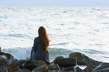 Image showing A lonely girl sits on the rocks by the sea and looks into the distance