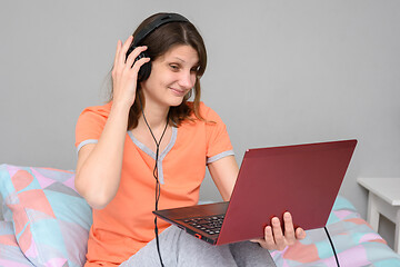 Image showing Girl straightens headphones while sitting on bed with laptop