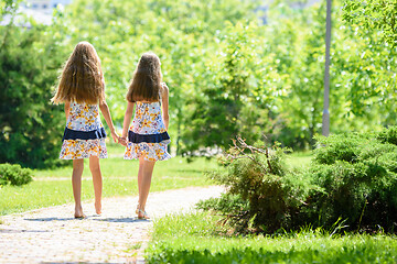 Image showing Girlfriends in identical clothes go by the handle in a city park