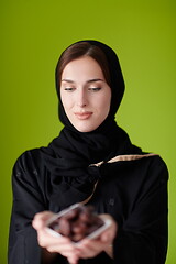 Image showing Woman in Abaya Holding a Date Fruit and glass of water