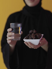 Image showing Woman in Abaya Holding a Date Fruit and glass of water