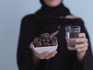 Image showing Woman in Abaya Holding a Date Fruit and glass of water