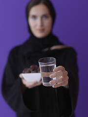 Image showing Woman in Abaya Holding a Date Fruit and glass of water