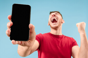 Image showing Young handsome man showing smartphone screen isolated on blue background in shock with a surprise face