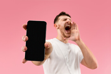 Image showing Young handsome man showing smartphone screen isolated on pink background in shock with a surprise face