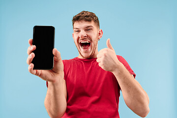 Image showing Young handsome man showing smartphone screen isolated on blue background in shock with a surprise face