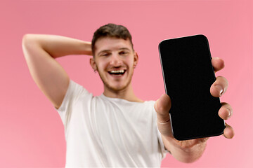 Image showing Young handsome man showing smartphone screen isolated on pink background in shock with a surprise face