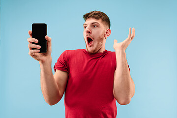 Image showing Young handsome man showing smartphone screen isolated on blue background in shock with a surprise face