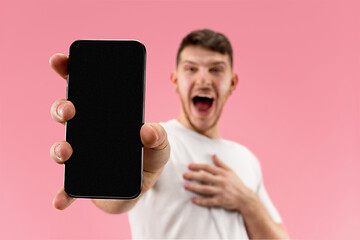 Image showing Young handsome man showing smartphone screen isolated on pink background in shock with a surprise face
