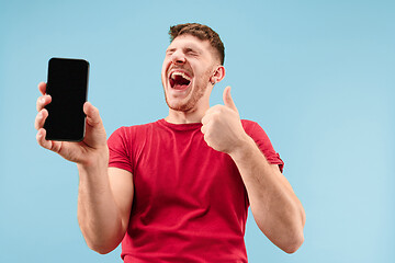 Image showing Young handsome man showing smartphone screen isolated on blue background in shock with a surprise face