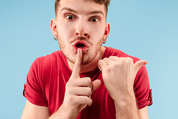 Image showing The young man whispering a secret behind her hand over blue background