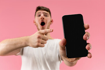 Image showing Young handsome man showing smartphone screen isolated on pink background in shock with a surprise face