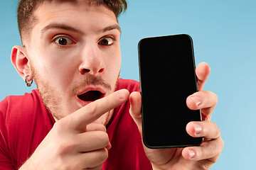 Image showing Young handsome man showing smartphone screen isolated on blue background in shock with a surprise face