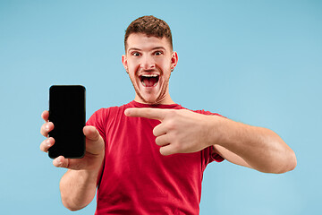 Image showing Young handsome man showing smartphone screen isolated on blue background in shock with a surprise face