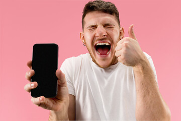 Image showing Young handsome man showing smartphone screen isolated on pink background in shock with a surprise face