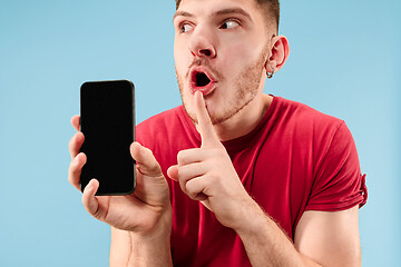 Image showing Young handsome man showing smartphone screen isolated on blue background in shock with a surprise face