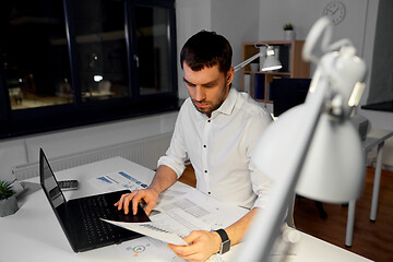 Image showing businessman with papers and laptop at night office