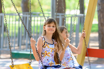 Image showing Two girls swing on a swing in a city park