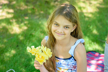 Image showing A tousled girl sits in a clearing and holds a bouquet of yellow roses