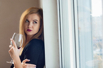 Image showing portrait of a girl looking sadly out the window with wine in her hands