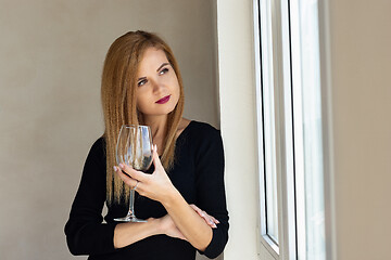 Image showing The girl stands thoughtfully at the window with a glass of red wine
